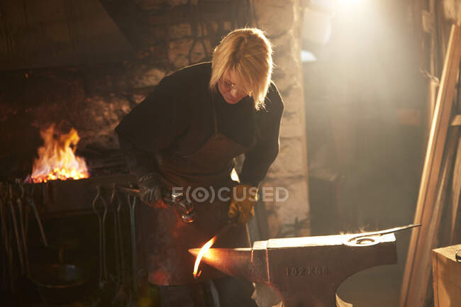 Female blacksmith forging steel in workshop — Stock Photo