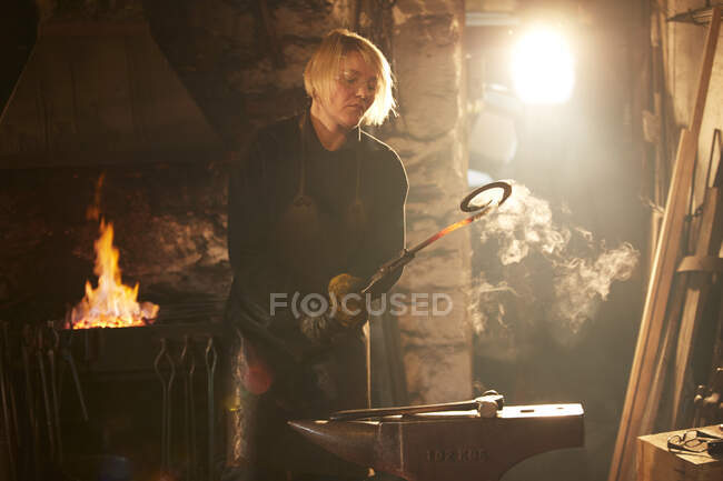 Female blacksmith working in sunny workshop — Stock Photo