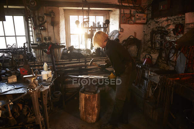 Female blacksmith working at anvil in workshop — Stock Photo