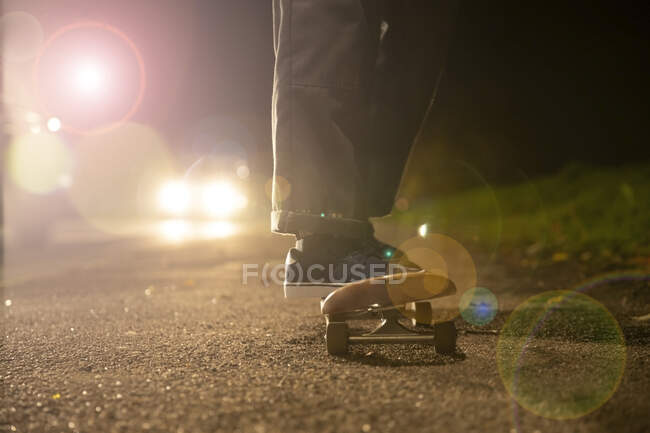 Junger Mann mit Skateboard im Scheinwerferlicht am Straßenrand — Stockfoto