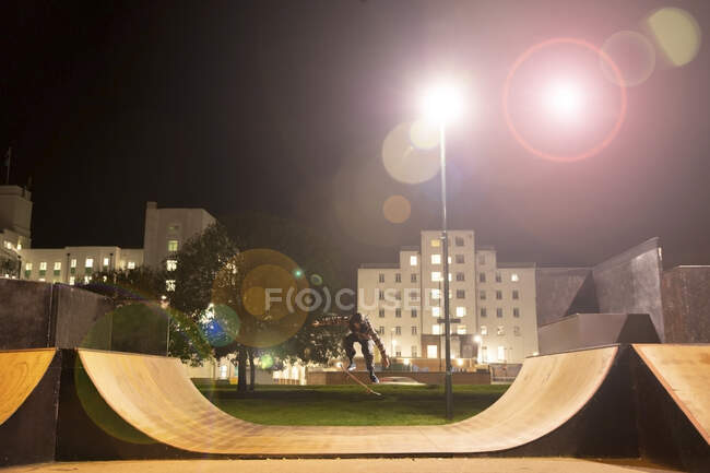 Joven monopatín en la rampa del parque de skate por la noche - foto de stock