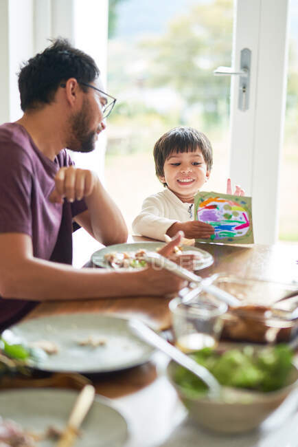 Padre e hijo comiendo y coloreando en la mesa - foto de stock