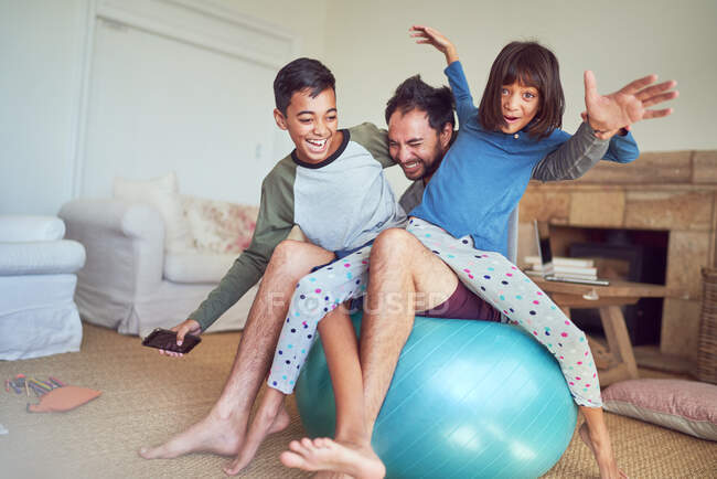 Retrato familia feliz jugando en la pelota de fitness en la sala de estar - foto de stock