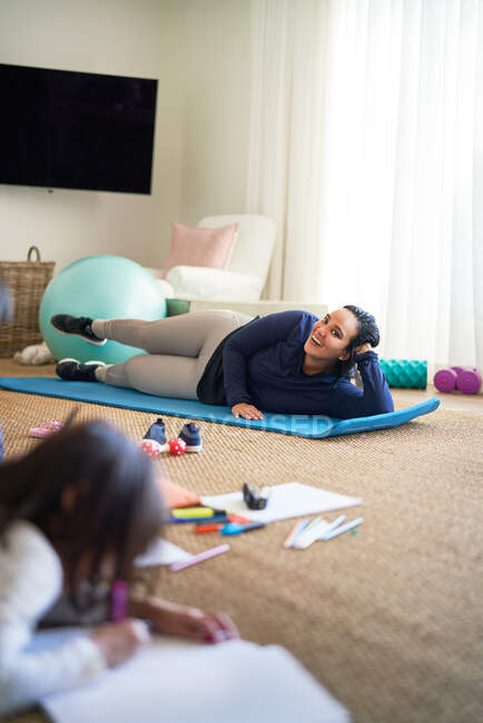 Smiling mother exercising while daughter draws in living room — Stock Photo