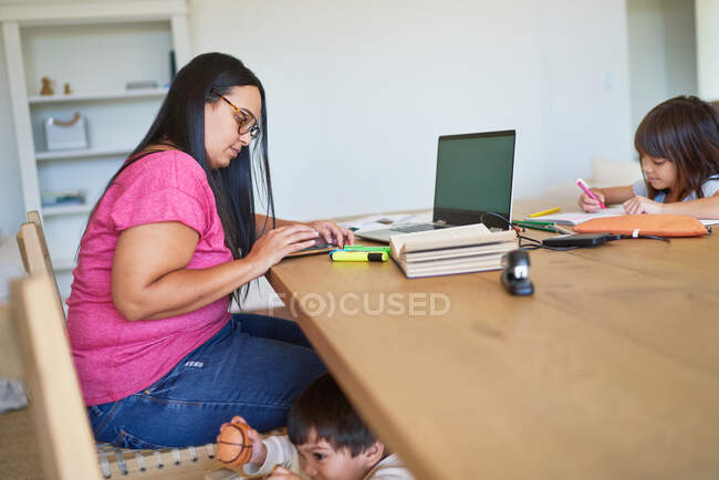 Bambini che giocano e fanno i compiti mentre la madre lavora a tavola — Foto stock