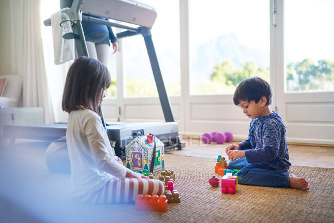 Kids playing with toys on floor by mother on treadmill — Stock Photo
