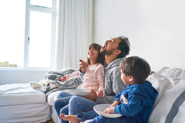 Игривая семья ест попкорн на диване — стоковое фото