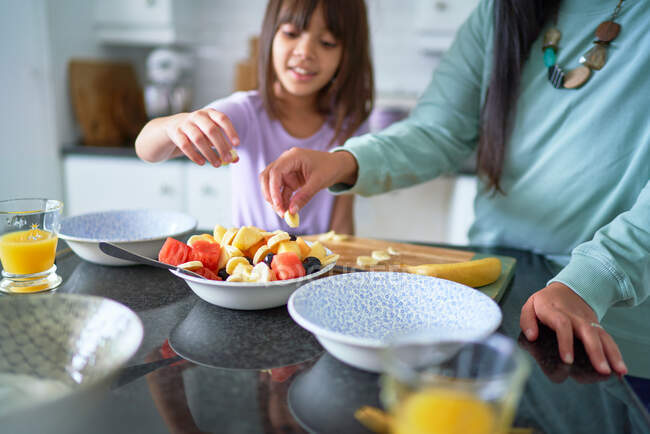 Mother and daughter eating fruit in kitchen — Stock Photo