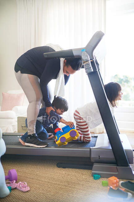 Kids with toys distracting mother on treadmill — Stock Photo