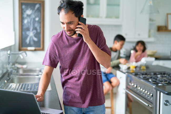 Man working at laptop in kitchen with kids — Stock Photo
