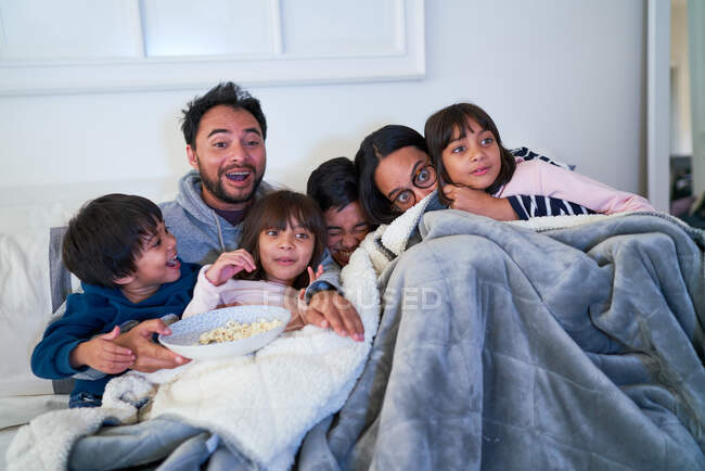Family cuddling and watching scary movie on sofa — Stock Photo