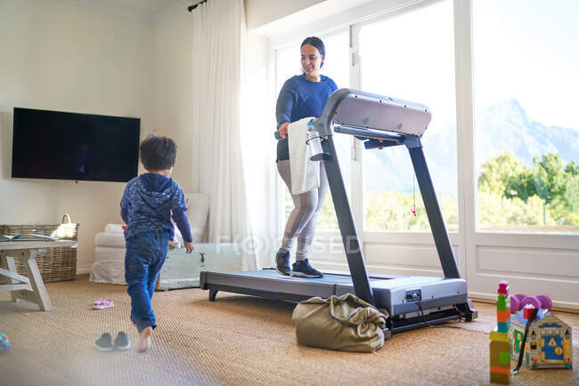 Junge spielt im Wohnzimmer, während Mama auf Laufband turnt — Stockfoto