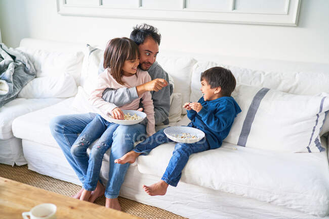 Батько і діти їдять попкорн на дивані у вітальні — стокове фото