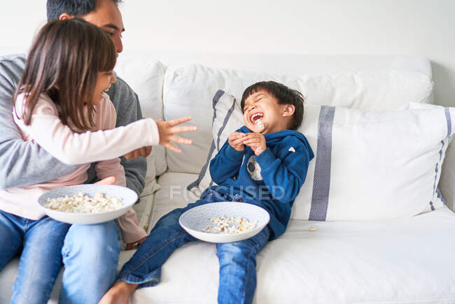 Familia juguetona con palomitas de maíz en el sofá de la sala - foto de stock