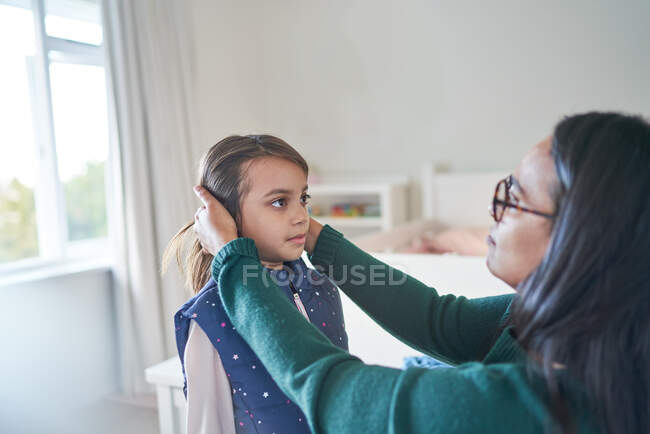 Madre ayudando a su hija a arreglar el cabello - foto de stock