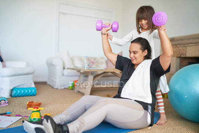 Daughter helping mother exercising with dumbbells in living room — Stock Photo