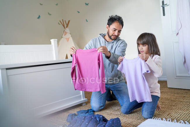 Father and daughter folding clothes in bedroom — Stock Photo