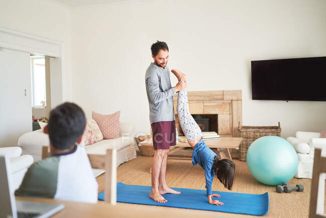 Padre aiuta la figlia a stare in piedi sul tappetino yoga in soggiorno — Foto stock