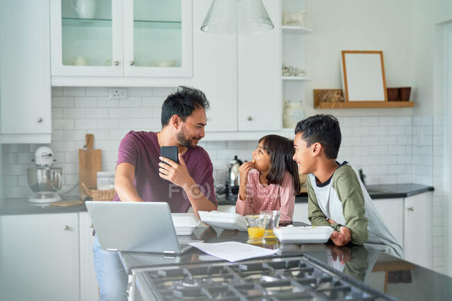 Father working in kitchen with kids eating takeout food — Stock Photo