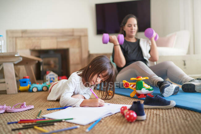 Filha colorir enquanto a mãe se exercita na sala de estar — Fotografia de Stock