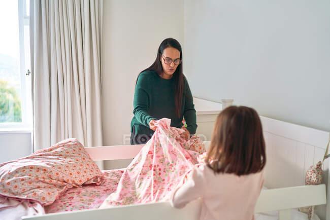 Mother helping daughter make bed — Stock Photo