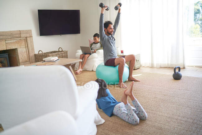 Padre haciendo ejercicio con mancuernas en la sala de estar con niños - foto de stock