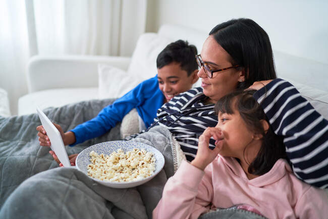 Madre e hijos con palomitas de maíz viendo películas en tabletas digitales - foto de stock