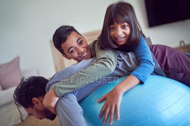 Portrait playful kids on top of father exercising on fitness ball — Stock Photo