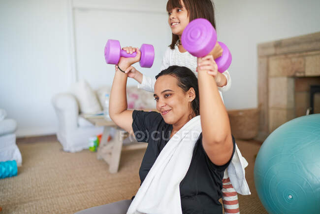 Daughter helping mother exercise with dumbbells in living room — Stock Photo