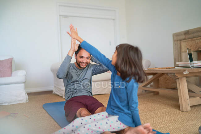 Feliz padre e hija chocando los cinco en la esterilla de yoga en la sala de estar - foto de stock