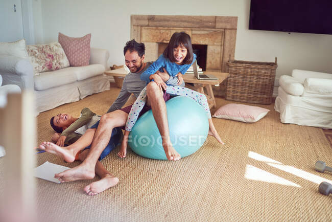 Padre juguetón e hijos en la pelota de fitness en la sala de estar - foto de stock