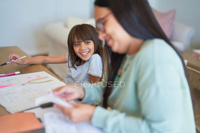 Menina feliz colorir ao lado da mãe pagar contas na mesa de jantar — Fotografia de Stock