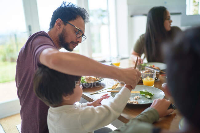 Father helping son cut food at dinner table — Stock Photo