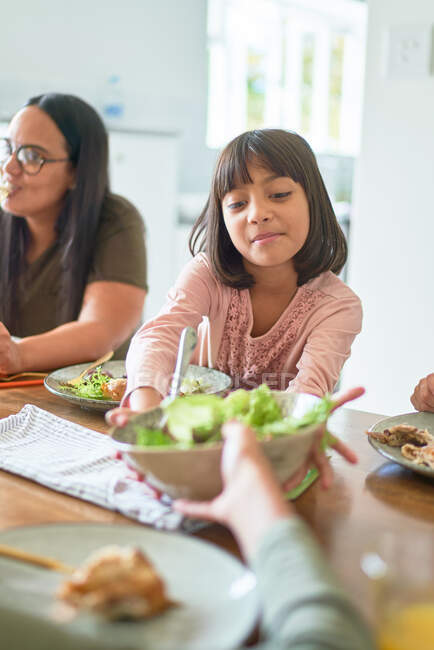 Girl reaching for salad at lunch table — Stock Photo