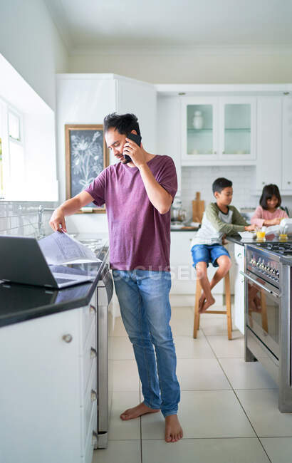 Father working at laptop in kitchen with kids eating — Stock Photo
