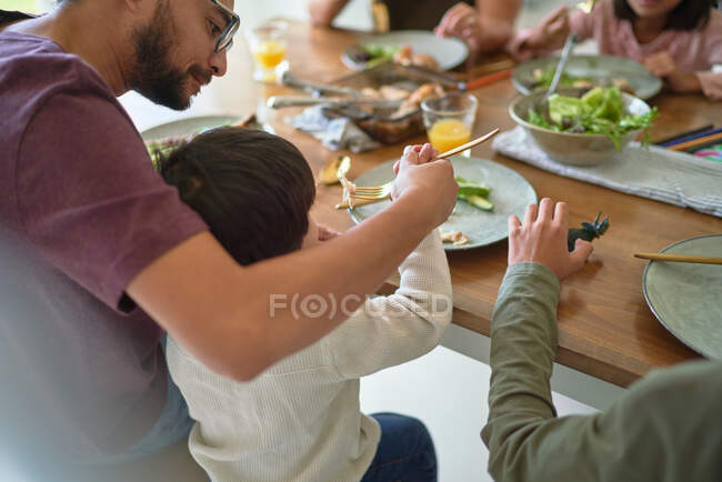 Father feeding toddler son at dinner table — Stock Photo