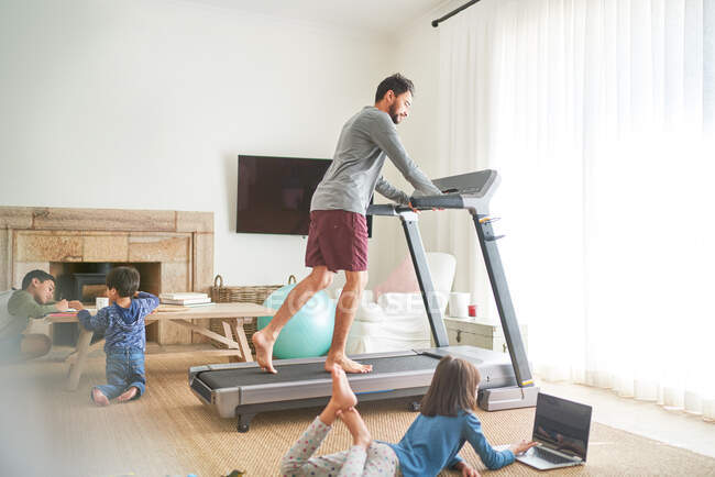 Father exercising on treadmill in living room with kids — Stock Photo