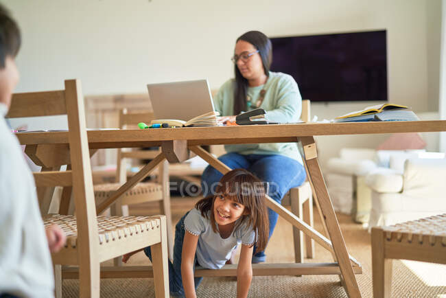 Kinder spielen unter Mutter, die am Esstisch arbeitet — Stockfoto