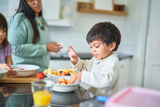 Lindo chico comiendo fruta fresca en la cocina - foto de stock