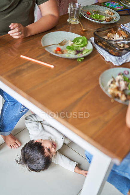 Мальчик играет под обеденным столом — стоковое фото