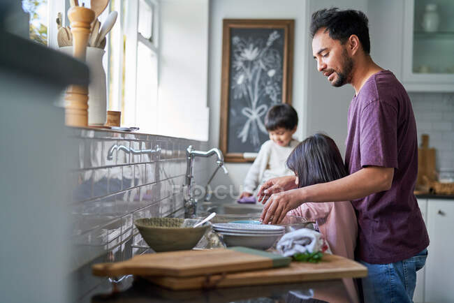 Pai e crianças fazendo pratos na pia da cozinha — Fotografia de Stock
