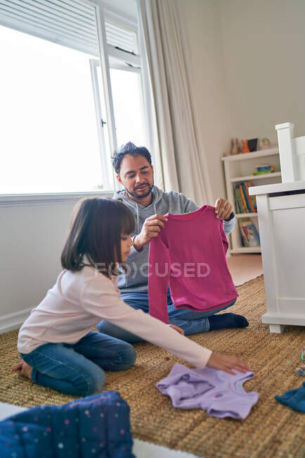 Father helping daughter fold clothes in bedroom — Stock Photo