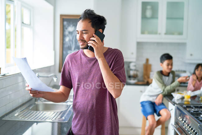 Father talking on smart phone in kitchen with kids — Stock Photo