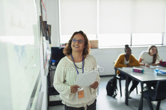 Profesor sonriente dirigiendo la lección en la pantalla de proyección en el aula - foto de stock