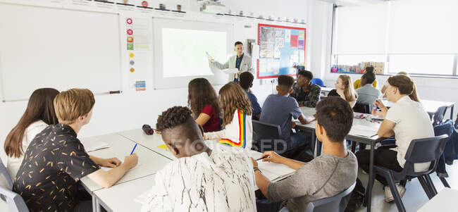 Étudiants du secondaire regardant l'enseignant à l'écran de projection pendant la leçon en classe — Photo de stock