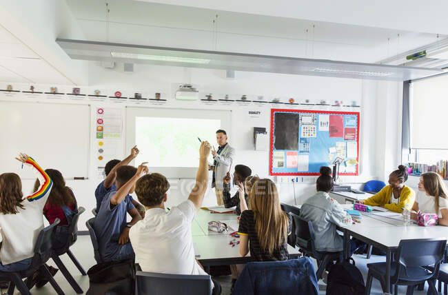 Учитель средней школы обращается к ученикам с поднятыми руками во время урока в классе — стоковое фото