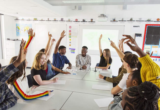 Estudiantes de secundaria con las manos levantadas en la clase de debate - foto de stock