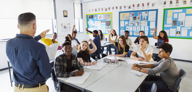 High school teacher calling on students with hands raised in classroom — Stock Photo
