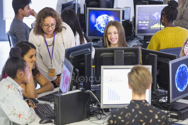Junior high teacher helping students using computers in computer lab — Stock Photo