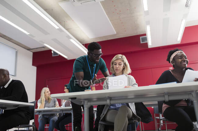 Instrutor universitário comunitário ajudando estudante com papelada em sala de aula — Fotografia de Stock